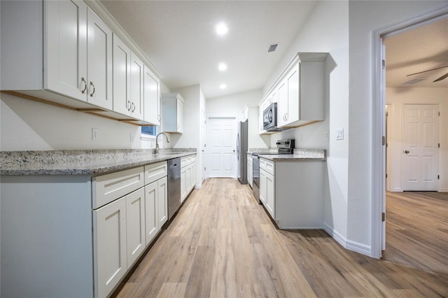 kitchen with light stone counters, white cabinetry, stainless steel appliances, and light hardwood / wood-style floors