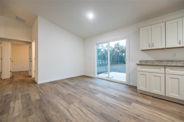 unfurnished dining area featuring lofted ceiling and light wood-type flooring