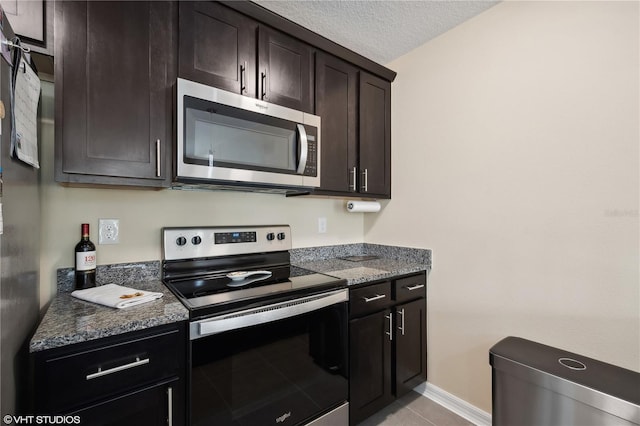 kitchen with light tile patterned floors, appliances with stainless steel finishes, dark brown cabinetry, a textured ceiling, and dark stone counters