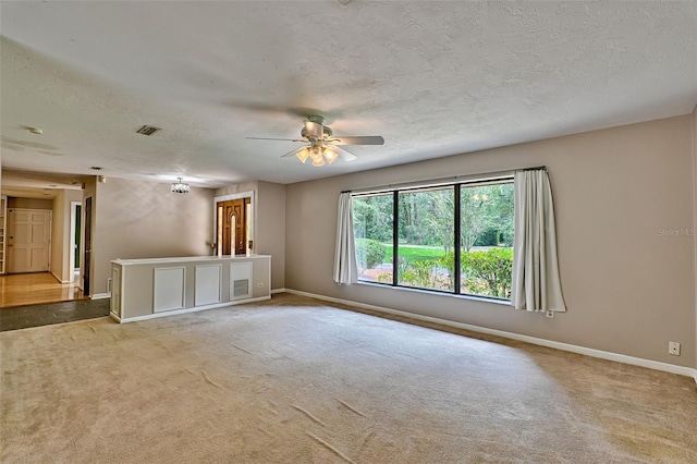 unfurnished living room with a ceiling fan, visible vents, carpet, baseboards, and a textured ceiling