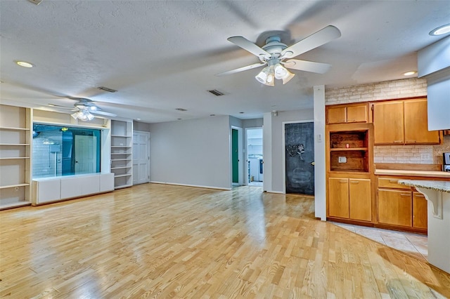 kitchen with visible vents, light wood finished floors, a ceiling fan, backsplash, and light countertops