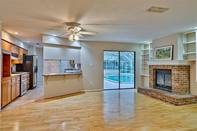 kitchen with visible vents, light wood finished floors, ceiling fan, appliances with stainless steel finishes, and a kitchen breakfast bar