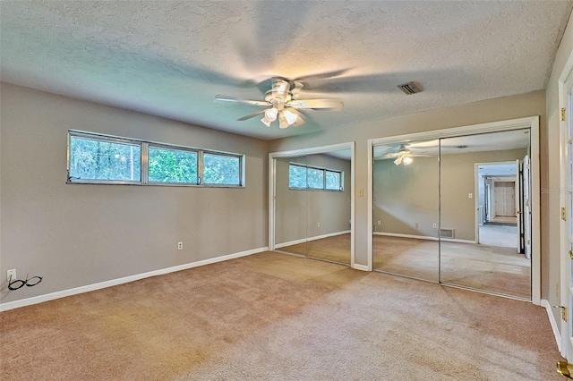 unfurnished bedroom featuring carpet flooring, visible vents, and two closets