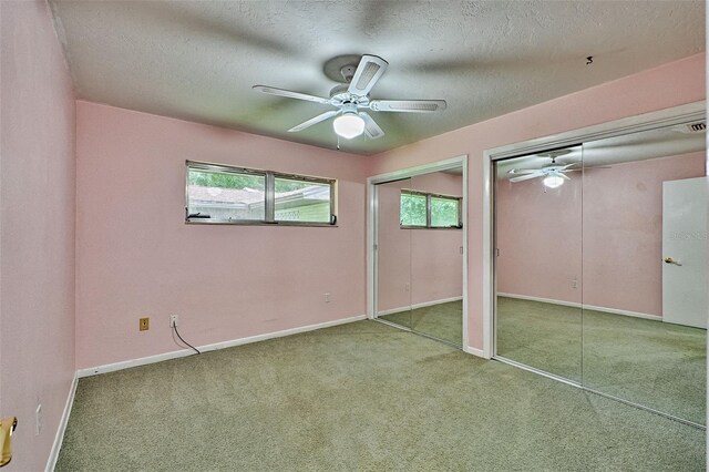 unfurnished bedroom with carpet flooring, baseboards, multiple closets, and a textured ceiling