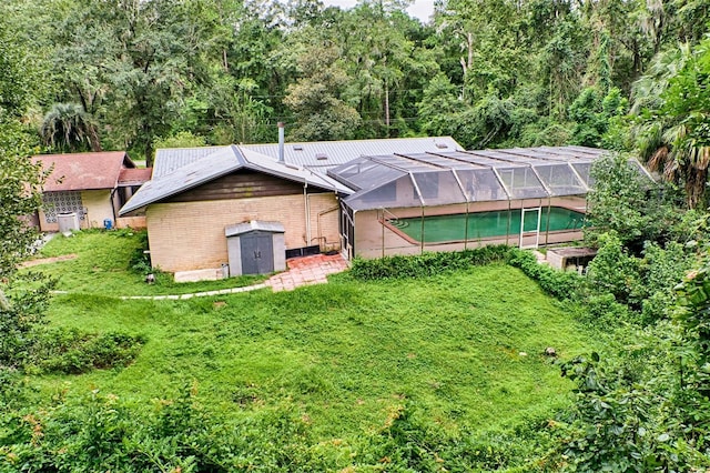 back of house with a lanai, an outdoor pool, brick siding, and a yard