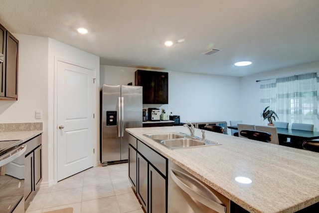 kitchen featuring light tile patterned floors, sink, dark brown cabinets, a center island with sink, and stainless steel appliances