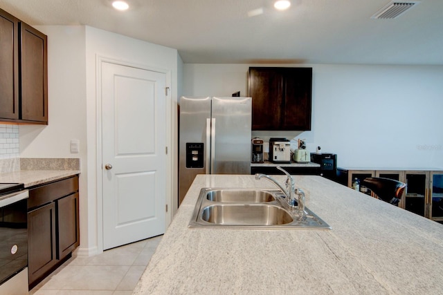 kitchen featuring stainless steel fridge, electric range oven, light tile patterned floors, dark brown cabinets, and sink