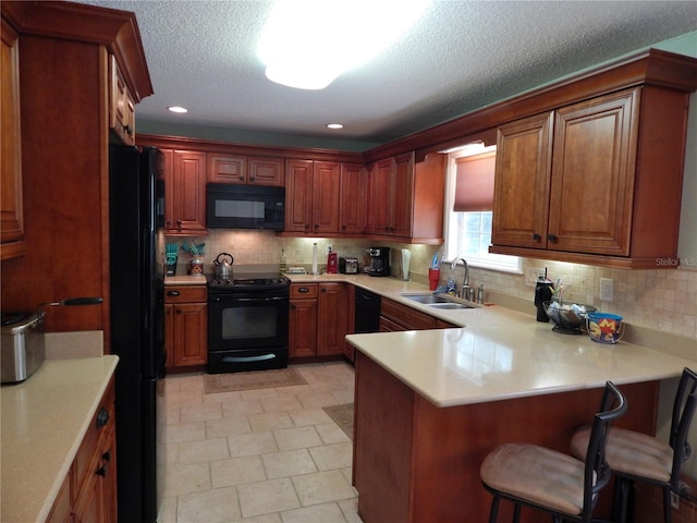 kitchen featuring a textured ceiling, sink, black appliances, kitchen peninsula, and a breakfast bar