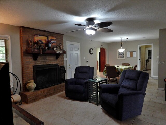 living room with a textured ceiling, ceiling fan, light tile patterned floors, and a fireplace