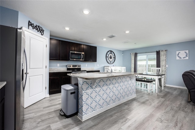 kitchen with appliances with stainless steel finishes, a kitchen island with sink, sink, and light hardwood / wood-style flooring