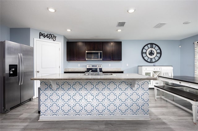 kitchen with light hardwood / wood-style floors, a kitchen island with sink, sink, and stainless steel appliances