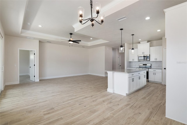 kitchen featuring white cabinets, a kitchen island, appliances with stainless steel finishes, a tray ceiling, and ceiling fan with notable chandelier