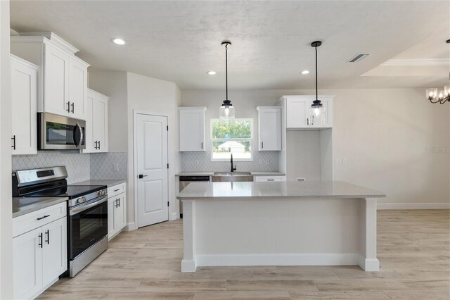 kitchen with decorative light fixtures, stainless steel appliances, white cabinets, and a center island