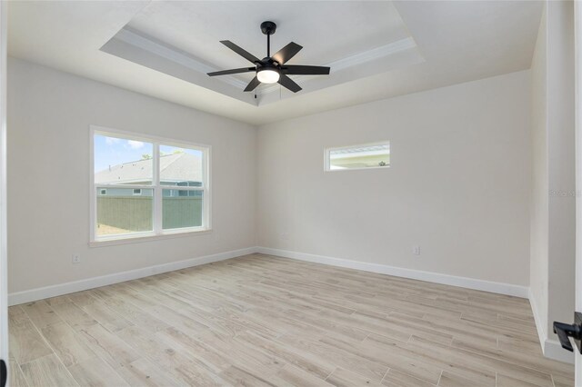 empty room with ceiling fan, a tray ceiling, light hardwood / wood-style floors, and a wealth of natural light