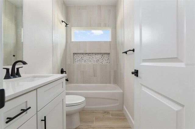 full bathroom featuring wood-type flooring, tiled shower / bath combo, vanity, and toilet