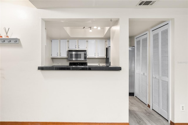 kitchen with light wood-type flooring, a raised ceiling, kitchen peninsula, and white cabinetry