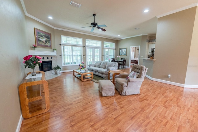 living room featuring ceiling fan, light wood-type flooring, crown molding, and a tile fireplace