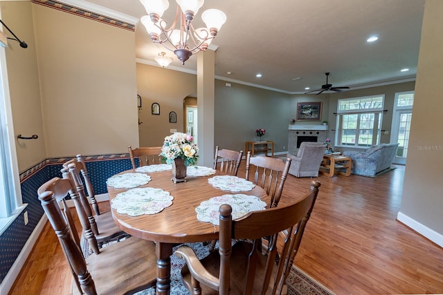 dining space featuring light hardwood / wood-style flooring, ceiling fan with notable chandelier, crown molding, and a tile fireplace