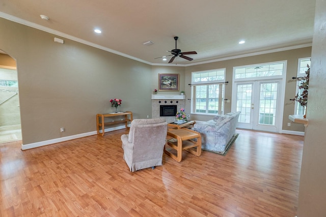 living room with light wood-type flooring, a tiled fireplace, crown molding, ceiling fan, and french doors