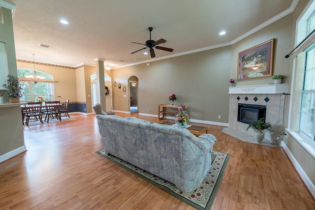 living room featuring ornamental molding, ceiling fan with notable chandelier, hardwood / wood-style floors, and a tile fireplace