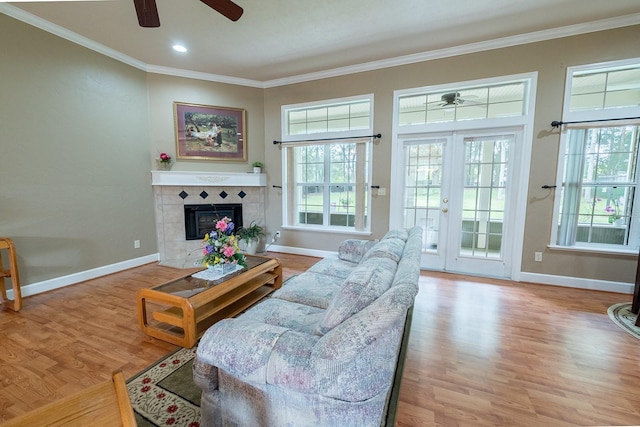 living room featuring light wood-type flooring, a tiled fireplace, ceiling fan, and a healthy amount of sunlight