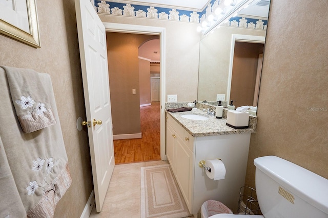 half bath with toilet, wood finished floors, vanity, and baseboards