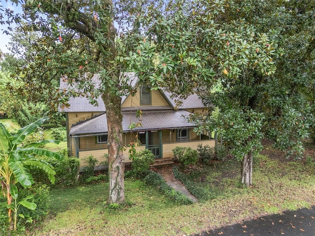 view of property hidden behind natural elements with a front yard and covered porch