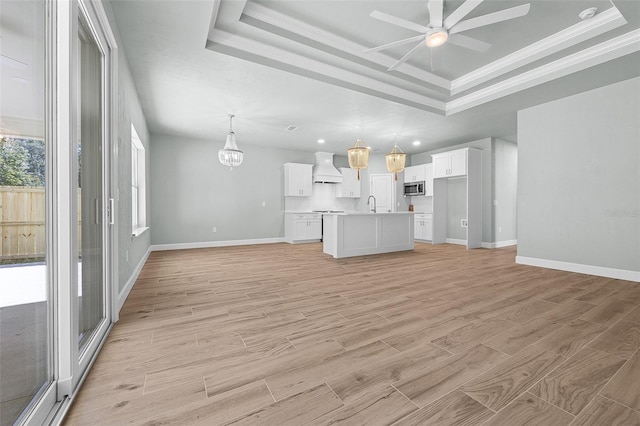 unfurnished living room with a tray ceiling, ceiling fan, light hardwood / wood-style flooring, ornamental molding, and sink