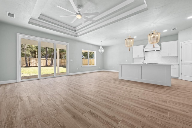 unfurnished living room with light hardwood / wood-style floors, a raised ceiling, ceiling fan, and sink