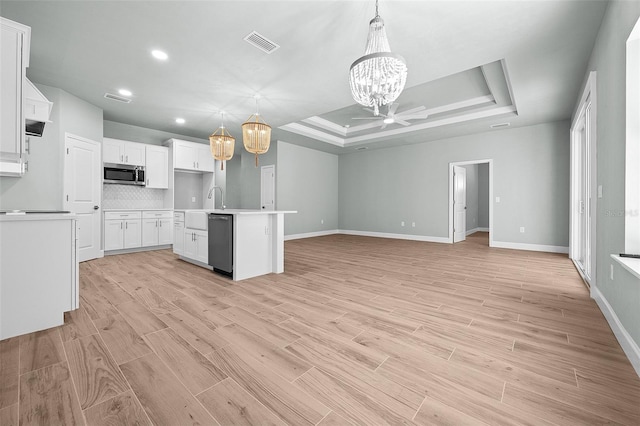 kitchen with a tray ceiling, light hardwood / wood-style floors, a center island with sink, appliances with stainless steel finishes, and decorative light fixtures