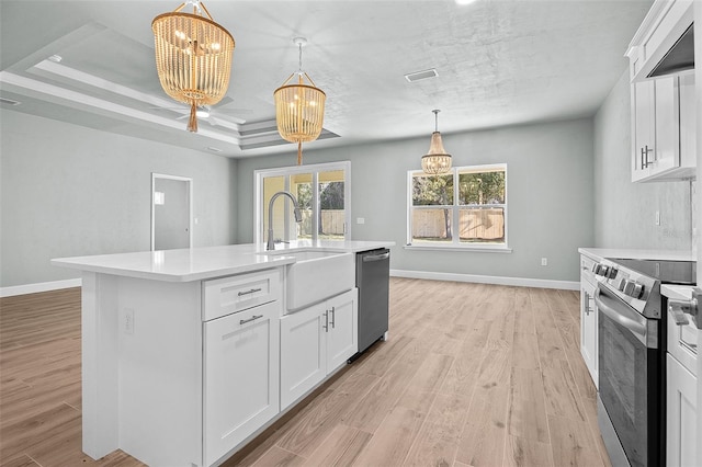 kitchen with appliances with stainless steel finishes, light hardwood / wood-style floors, white cabinets, an inviting chandelier, and a center island with sink