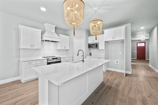 kitchen with white cabinets, custom exhaust hood, sink, stainless steel appliances, and a notable chandelier