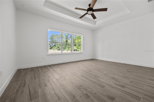 spare room featuring ornamental molding, wood-type flooring, ceiling fan, and a raised ceiling