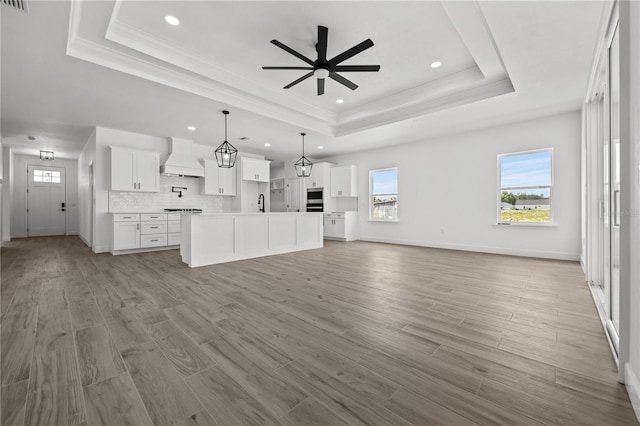 unfurnished living room with light wood-type flooring, a raised ceiling, crown molding, and ceiling fan