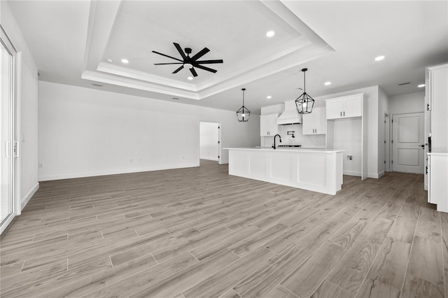 unfurnished living room featuring light wood-type flooring, ceiling fan, a raised ceiling, and sink