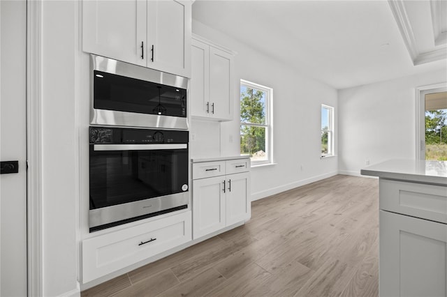 kitchen featuring a wealth of natural light, white cabinets, stainless steel double oven, and light wood-type flooring