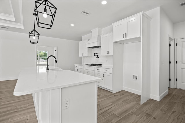 kitchen featuring a center island with sink, premium range hood, white cabinetry, and sink