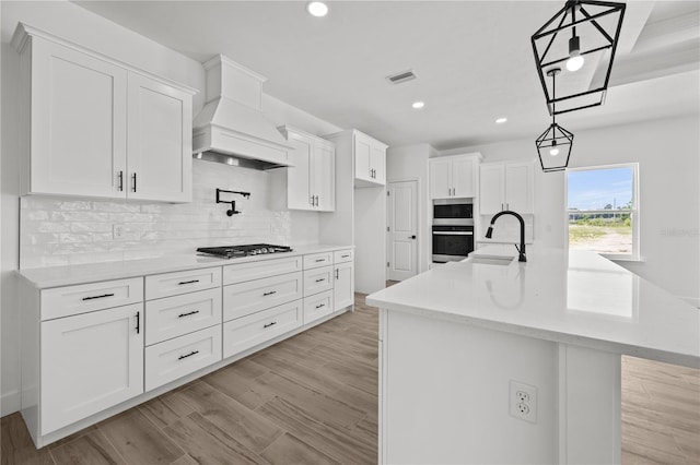 kitchen with an island with sink, hanging light fixtures, sink, and white cabinetry