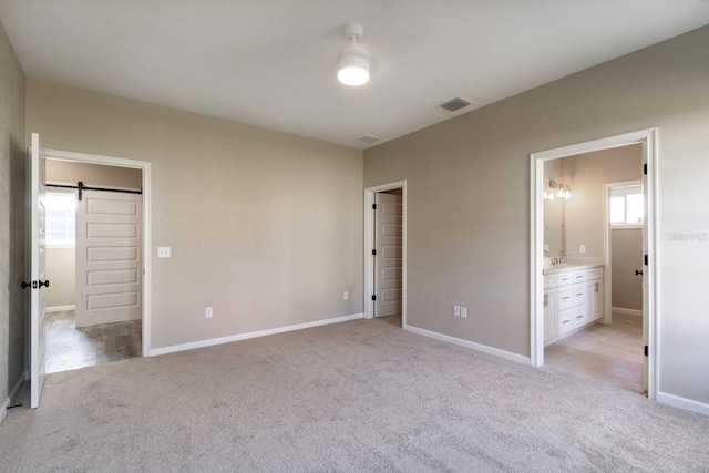 unfurnished bedroom featuring a barn door, light colored carpet, connected bathroom, and multiple windows