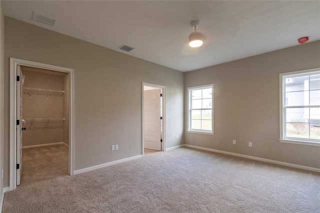 unfurnished bedroom with multiple windows, a spacious closet, a closet, and light colored carpet