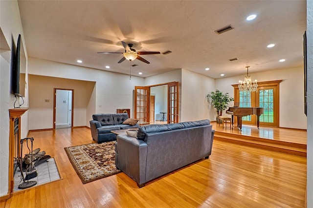 living room with ceiling fan with notable chandelier and light hardwood / wood-style flooring