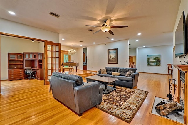 living room with ceiling fan with notable chandelier and light hardwood / wood-style flooring