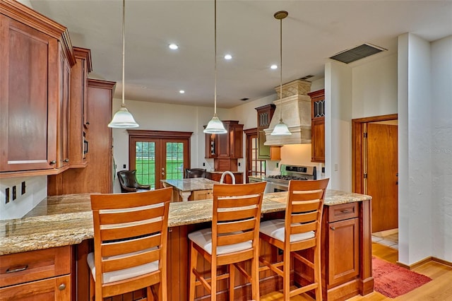 kitchen with pendant lighting, premium range hood, a kitchen breakfast bar, light hardwood / wood-style floors, and gas stove