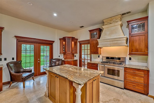 kitchen with a kitchen island, stainless steel gas stove, light stone countertops, french doors, and premium range hood