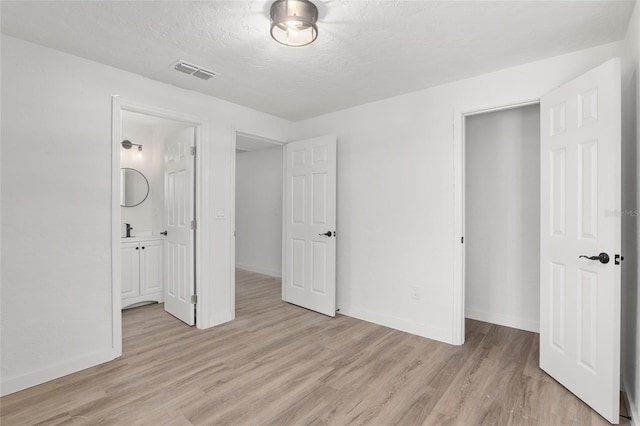 unfurnished bedroom with a textured ceiling, connected bathroom, and light hardwood / wood-style flooring