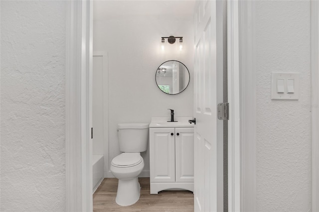 full bath with toilet, a textured wall, wood finished floors, and vanity