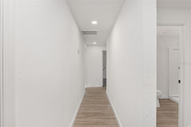 hallway featuring light wood-type flooring, baseboards, visible vents, and recessed lighting