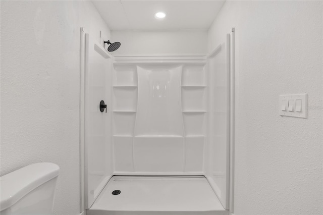 bathroom featuring toilet, a shower stall, and a textured wall