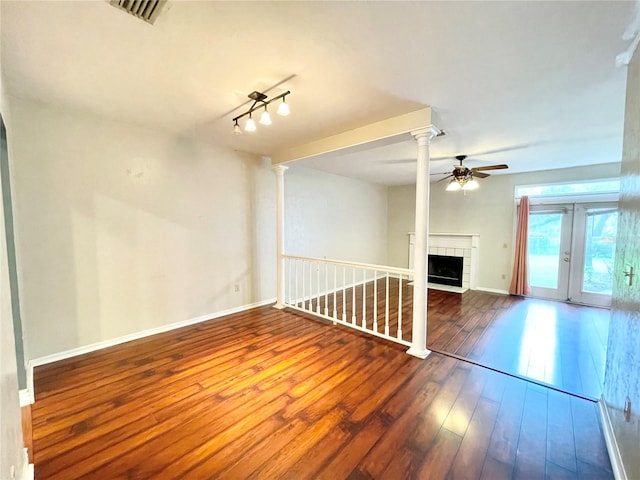 unfurnished living room featuring ceiling fan, hardwood / wood-style flooring, a tiled fireplace, and french doors