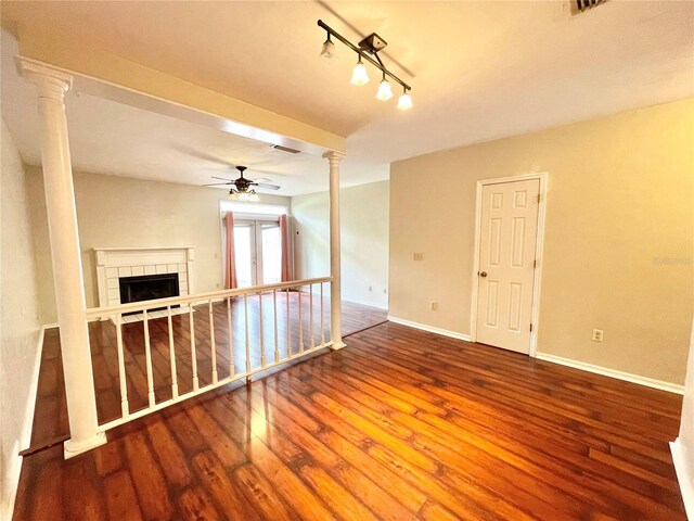 unfurnished room featuring wood-type flooring, a fireplace, ceiling fan, and ornate columns